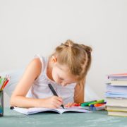 Amakids.bg-MentalnaAritmetika-AnglijskiEzik-GooglePlay-AppStore-education-concept-with-school-supplies-side-view-little-girl-drawing-copybook