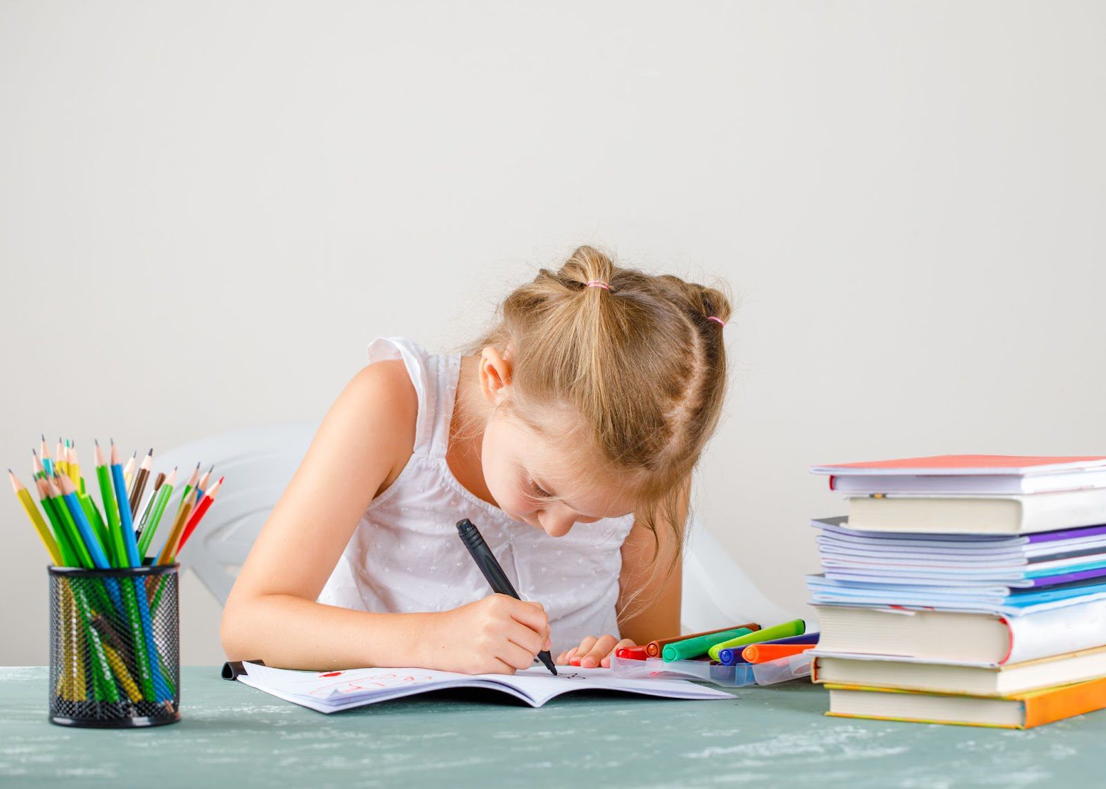 Amakids.bg-MentalnaAritmetika-AnglijskiEzik-GooglePlay-AppStore-education-concept-with-school-supplies-side-view-little-girl-drawing-copybook